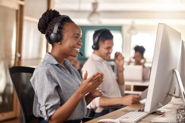 Call center, black woman and smile at computer for telemarketing, sales and support. Professional female consultant or agent with a headset and team for customer service, crm and help desk or advice