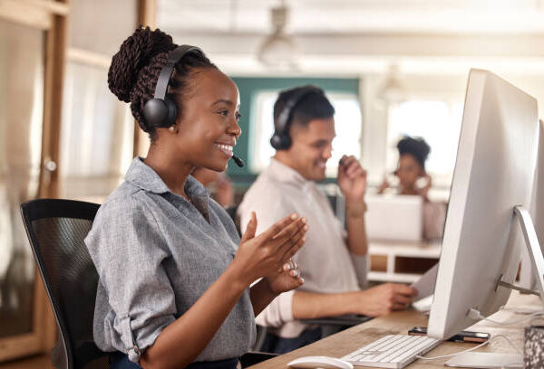 Call center, black woman and smile at computer for telemarketing, sales and support. Professional female consultant or agent with a headset and team for customer service, crm and help desk or advice